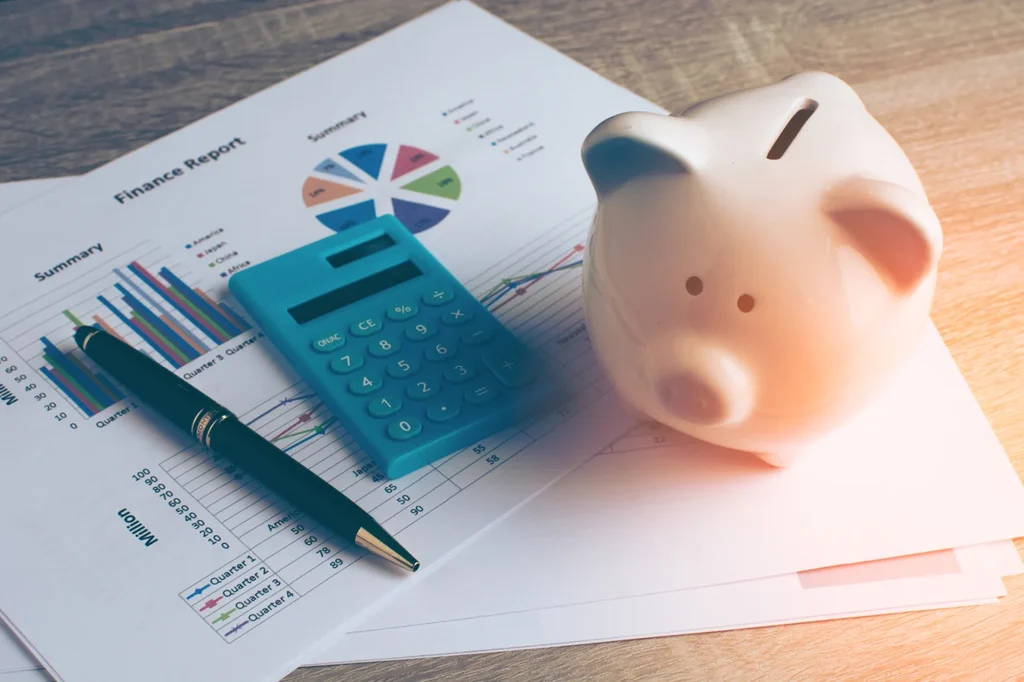 A set of computational graphs on paper, a pen, calculator, and a piggy bank.
