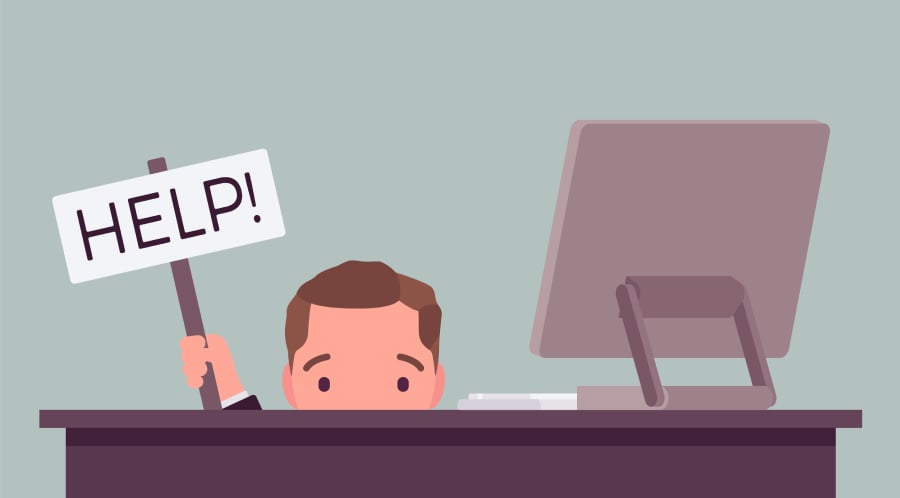 A man hinding behind his computer desk asking for help.