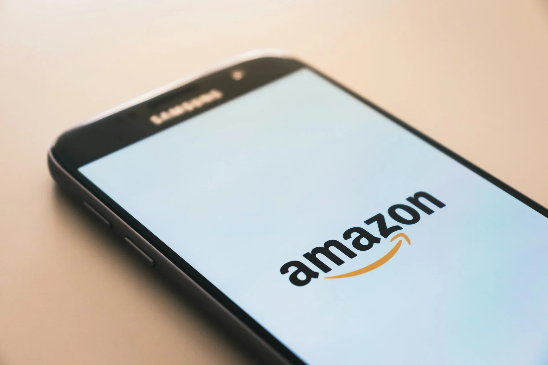 Smartphone displaying the Amazon logo on a white screen, resting diagonally on a beige surface.