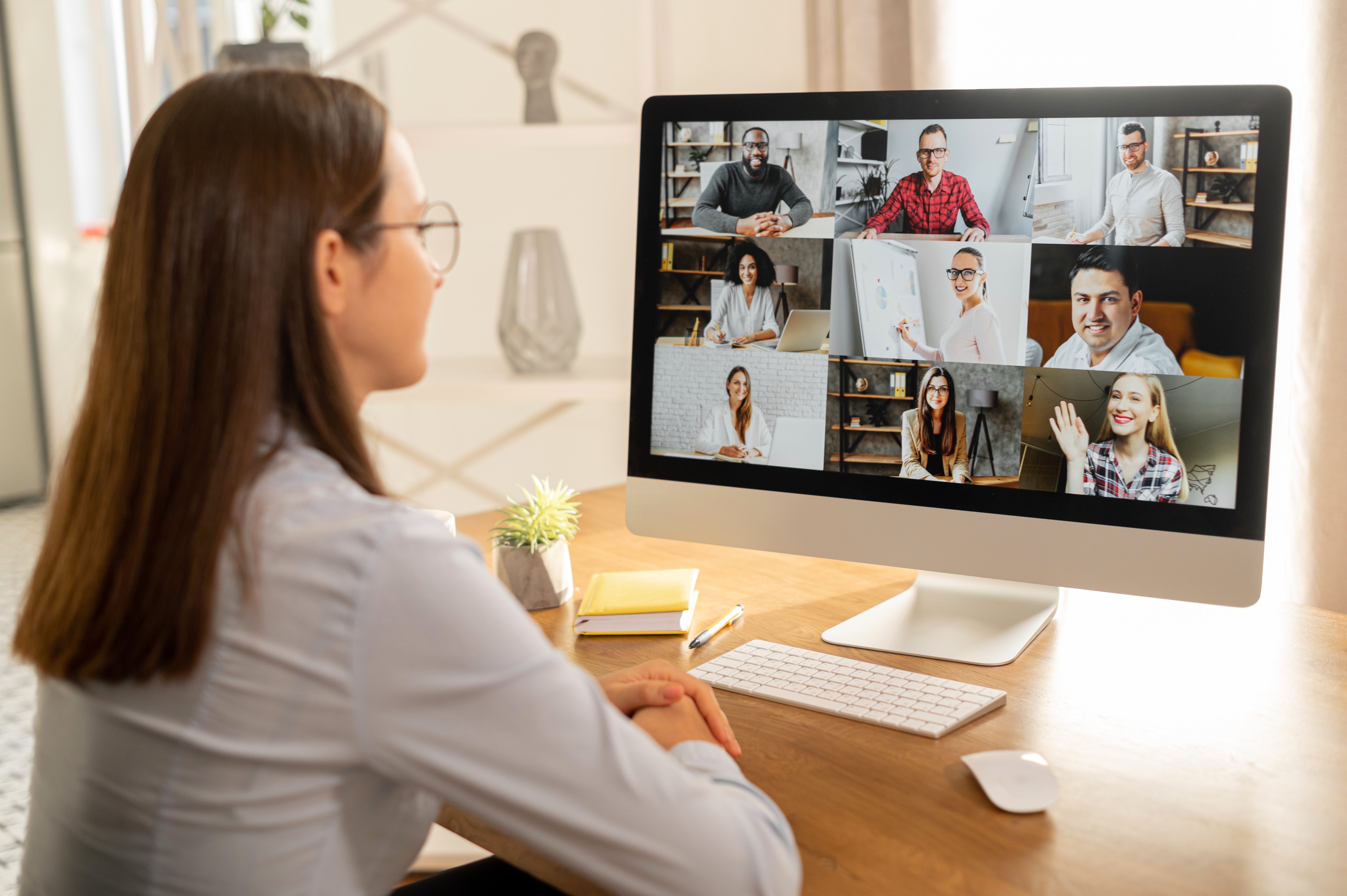 Woman sitting at a desk in front of a computer screen attending a video meeting with a group of other people.